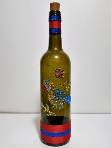 Bottle light featuring a jewelled parrot and red and blue ribbons.