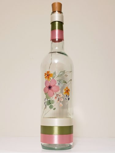 Bottle light featuring a waxy floral arrangement in rose, orange and green tones.